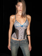 Model wearing a zebra print top with blue accents and jeans on a black background